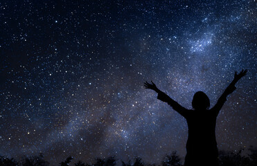 Silhouette of person raising arms under starry night sky with milky way symbolizing freedom and awe