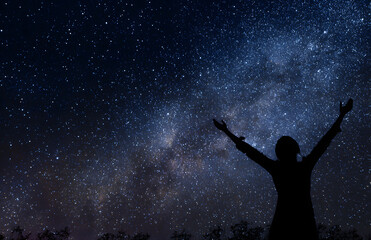 Silhouette of person raising arms under starry night sky with milky way symbolizing freedom and awe