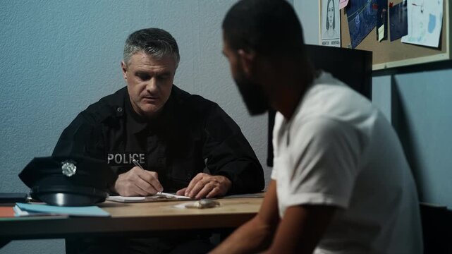 Police officer interrogating male witness in investigation office, writing notes