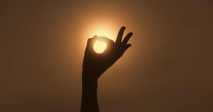 Sun Shines Through Meditative Hand Gesture in Serene Silhouette Shot