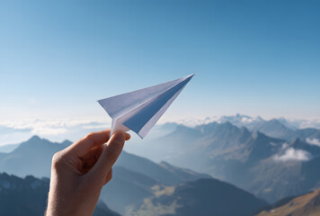Hand holding paper airplane against blue sky and mountain landscape symbolizing freedom and new beginnings