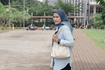 A young Indonesian Muslim woman standing on the side of the road to cross the road
