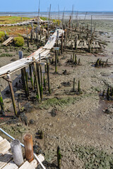 Old, weathered wooden walkway on stilts at the Palafita da Carrasqueira fishing port in Comporta, Portugal, stretching over muddy estuary.
