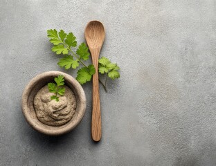 A wooden spoon rests near a bowl filled with a creamy spread and fresh herbs.