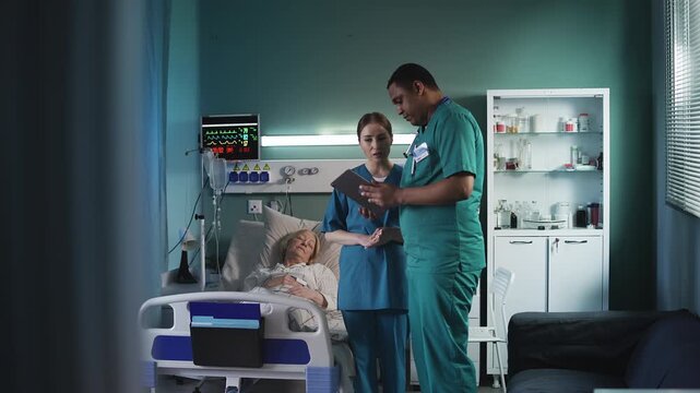 Male and female doctors discussing senior patient treatment plan using tablet