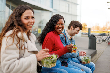 Group of multiethnic students sharing salads and smiling on campus street