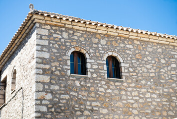 Traditional Greek stone house with arched windows and wooden shutters, Mediterranean architecture, sunny summer scene, exterior view