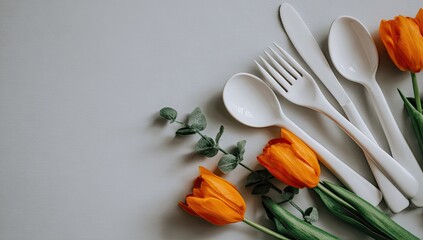 White cutlery and orange tulips arranged on a pale surface.
