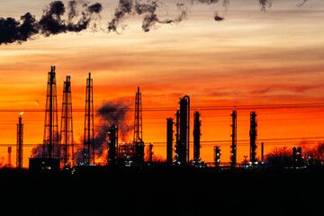 Obraz premium Close-up of towers and smokestacks at Leuna chemical plant at sunset, smoke and steam rising into an orange-yellow sky, highlighting heavy industry in Germany.