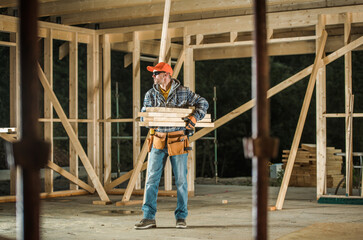 Fototapeta premium Construction Worker Carries Wooden Planks in Building Site During Daylight Hours