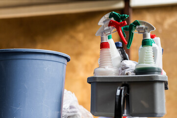 Cleaning supplies are arranged in a caddy near a blue bucket for home cleaning tasks on a sunny day