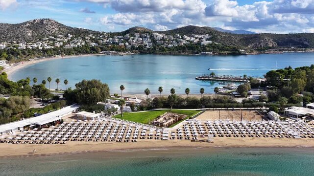 Aerial drone cinematic video of amazing organized sandy celebrity beach of Asteras featuring Temple of Apollo Zoster a true ancient cultural heritage, Vouliagmeni, Athens riviera, Greece