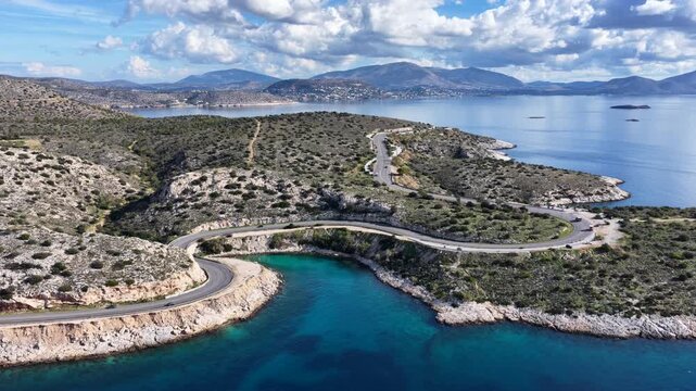 Aerial drone cinematic video of serpent seaside road forming small coves known as "Limanakia" next to famous Asteras Peninsula and lake Vouliagmenis, Athens Riviera, Attica, Greece