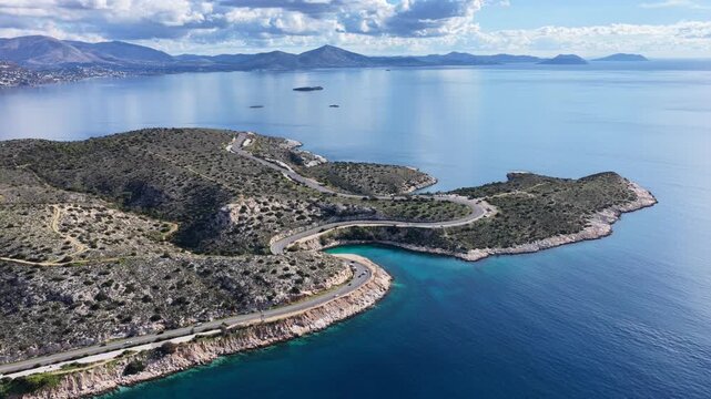 Aerial drone cinematic video of serpent seaside road forming small coves known as "Limanakia" next to famous Asteras Peninsula and lake Vouliagmenis, Athens Riviera, Attica, Greece