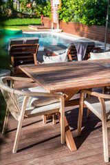 Outdoor dining area with wooden table and poolside view, surrounded by chairs in a sunny setting