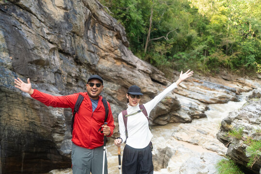 Two asian hiker stands on a light colored rock beside a gentle flowing stream are enjoy their hiking trip is look very happy to have reached their destination.
