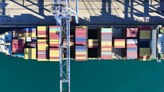 Aerial drone top down cinematic video of huge fully loaded Container ship anchored in loadingunloading logistics terminal port