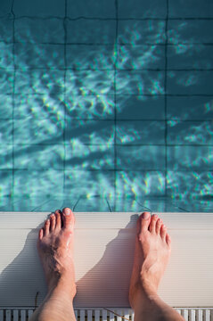 Feet at the edge of a swimming pool on a sunny day with water reflections visible