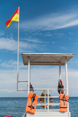 Fototapeta premium Lifeguard tower stands on a beach with orange life jackets and a flag flying on a sunny day by the sea