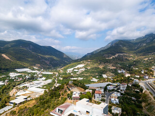 Aerial View of a Lush Green Mountain Valley with Agricultural Greenhouses, Scattered Residential Buildings, and a Winding Highway