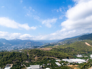 Vast Panoramic View of Green Pine-Covered Mountains and Hills Overlooking a Coastal City Valley under a Bright Blue Sky