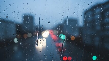 rain drops on window glass with blurred colorful bokeh lights in background city street at night during rainfall atmospheric moody weather scene abstract background