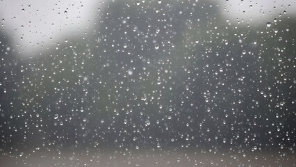 Closeup of raindrops on a window pane with a blurred, dark green outdoor background suggesting a rainy day or storm