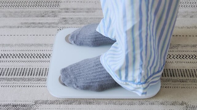 Person in pajamas steps off a weight scale with a measuring tape, achieving a weight loss goal