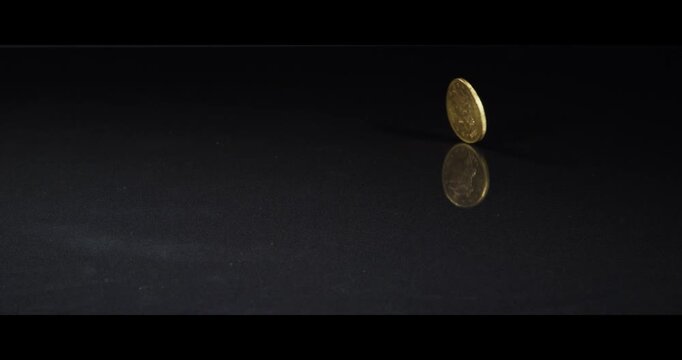 A gold coin is flicked onto a black reflective surface and spins continuously against a dark background, symbolizing chance, luck, gambling, and financial decision-making.