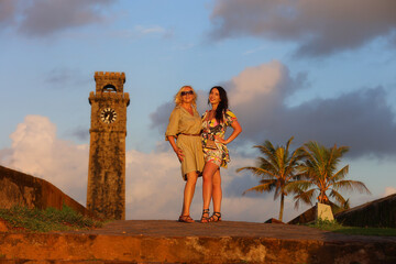 Two Women Posing by a Historic Clock Tower at Sunset