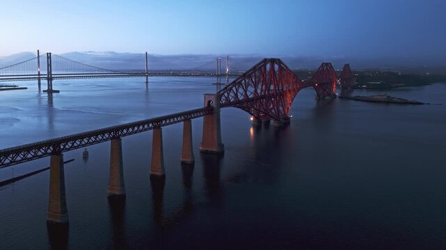 Aerial view of the iconic Forth Rail Bridge spanning the Firth of Forth in Scotland. Famous red steel railway structure, calm water, dramatic sky, and classic Scottish coastal landscape.