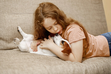 Happy girl and cute puppy dog, kissing and embracing with love and care on couch in lounge at home.