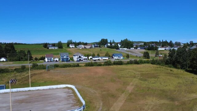 Video filmed by a drone that rises near the walls of an ice-free skating rink in summer to offer us an aerial view of a small rural farming village under a blue sky. Padoue, Quebec, Canada, 2025.