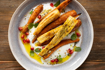 Top view of whole roasted carrots and parsnip slices on cheese on plate winter food