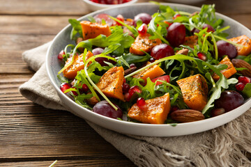 Salad with roasted pumpkin and grapes on plate wooden surface