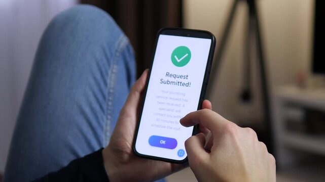 A closeup capturing a moment of relief: the smartphone screen shows a confirmed request sent to a plumber. This video perfectly illustrates the modern approach to solving home issues: fast, digital