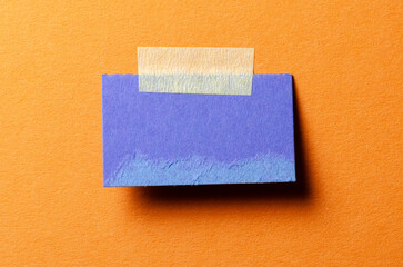 Piece of blank blue paper note with adhesive sticky tape and shadow on orange background