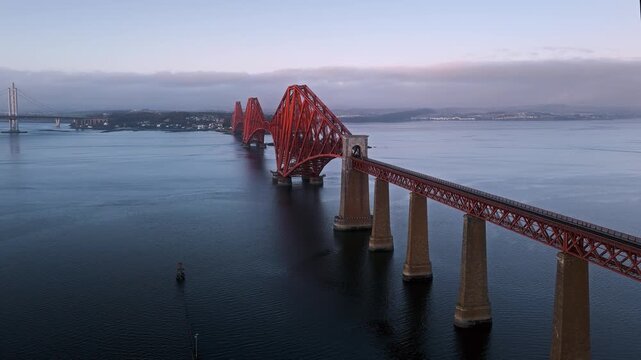 Aerial view of the iconic Forth Rail Bridge spanning the Firth of Forth in Scotland. Famous red steel railway structure, calm water, dramatic sky, and classic Scottish coastal landscape.