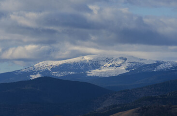 Fototapeta premium view of big snowed mountain peaks in winter and lower hills at bottom in sunny morning