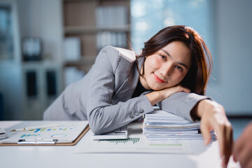 Asian businesswoman smiling resting head on paperwork pile