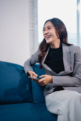 Asian businesswoman laughing and using smartphone on couch
