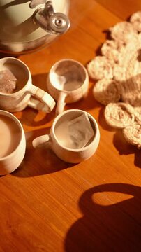 A table with four cups of tea and a teapot. The cups are arranged in a row and the teapot is in the middle