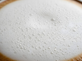 Frothy white foam topping a warm beverage with subtle brown undertones