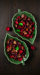 Two green leaf shaped dishes filled with dried potpourri on dark wood flowers petals