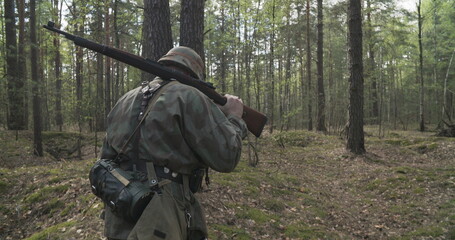 Reenactor Dressed As German Infantry Soldier Going By Forest In Slo-mo Motion -mo. Soldier With Carabines Mauser 98k Combing Forest Autumn Season. Wermacht Uniform. Reenactment Tactic Game