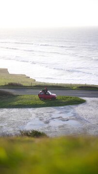 A red car is parked on a grassy hill overlooking the ocean. The scene is peaceful and serene, with the car and the ocean as the main focal points