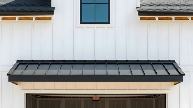 Modern farmhouse exterior white board and batten siding | Black standing seam metal awning over garage door opening | Architectural detail of white house facade and black roof elements 