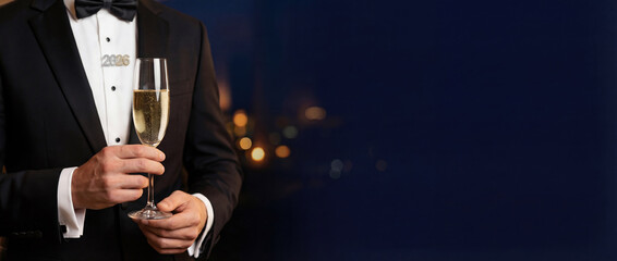 Elegant man in a black tuxedo holding a glass of champagne with a 2026 brooch. New Year's Eve celebration banner with night city background and copy space.