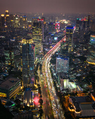 Drone aerial view of a vibrant capital city at night featuring illuminated skyscrapers and busy traffic below. Urban cityscape with glowing lights, modern architecture, and dynamic nighttime atmospher