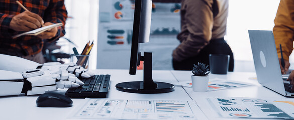 A vibrant office scene showcasing a robotic arm, laptop, and business charts while professionals engage in creative collaboration. Modern workspace inspires productivity and innovation.Noogenesis